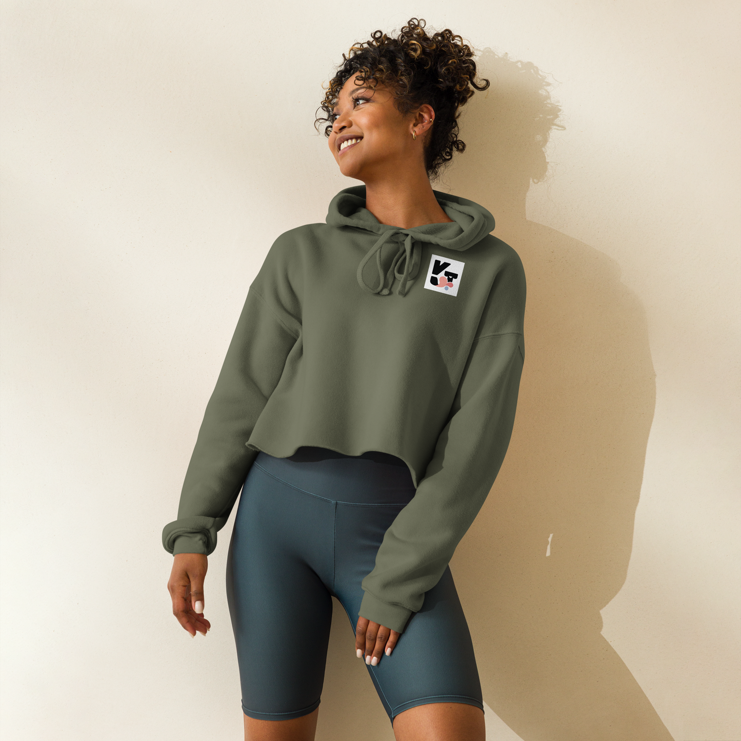 Kurzer Crop-Hoodie "Tunnelrumps" mit Logoaufdruck vom Hundesportmarke Klexgetier. Das Modell zeigt eine lächelnde Frau mit lockigem Haar, die den olivgrünen Pullover in einem hellen Ambiente trägt.