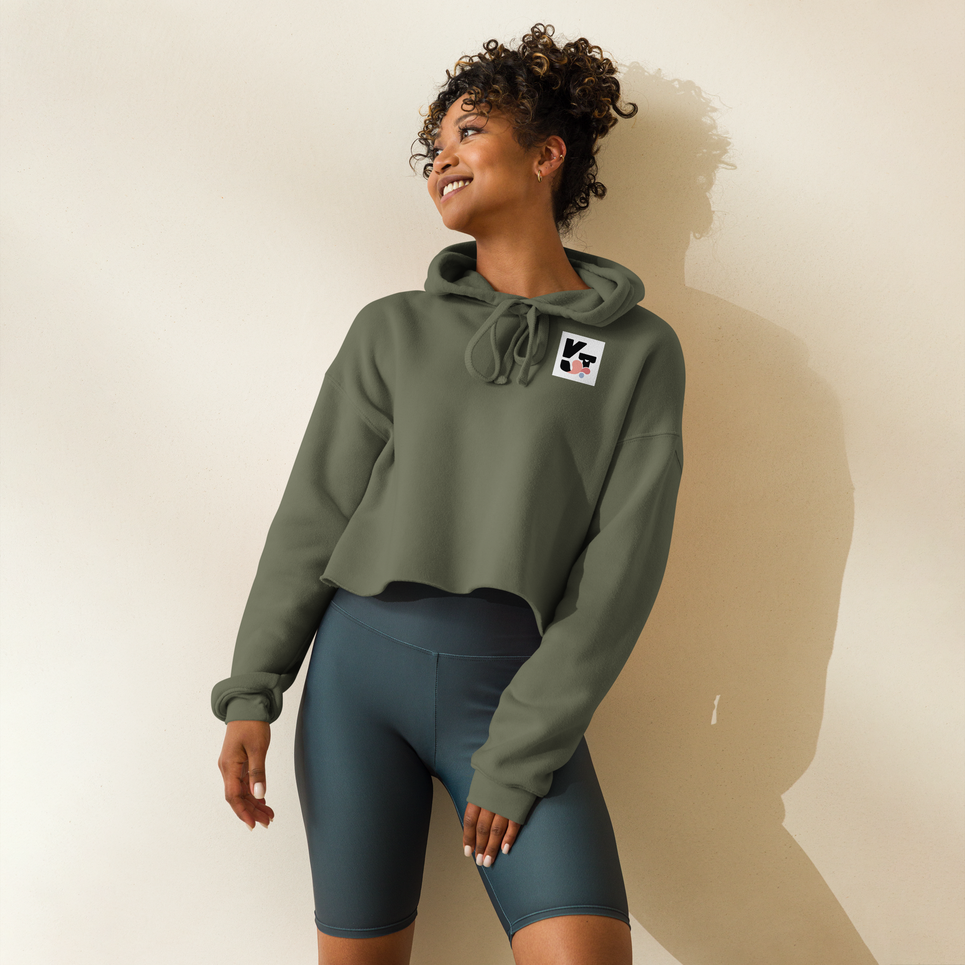 Kurzer Crop-Hoodie "Tunnelrumps" mit Logoaufdruck vom Hundesportmarke Klexgetier. Das Modell zeigt eine lächelnde Frau mit lockigem Haar, die den olivgrünen Pullover in einem hellen Ambiente trägt.
